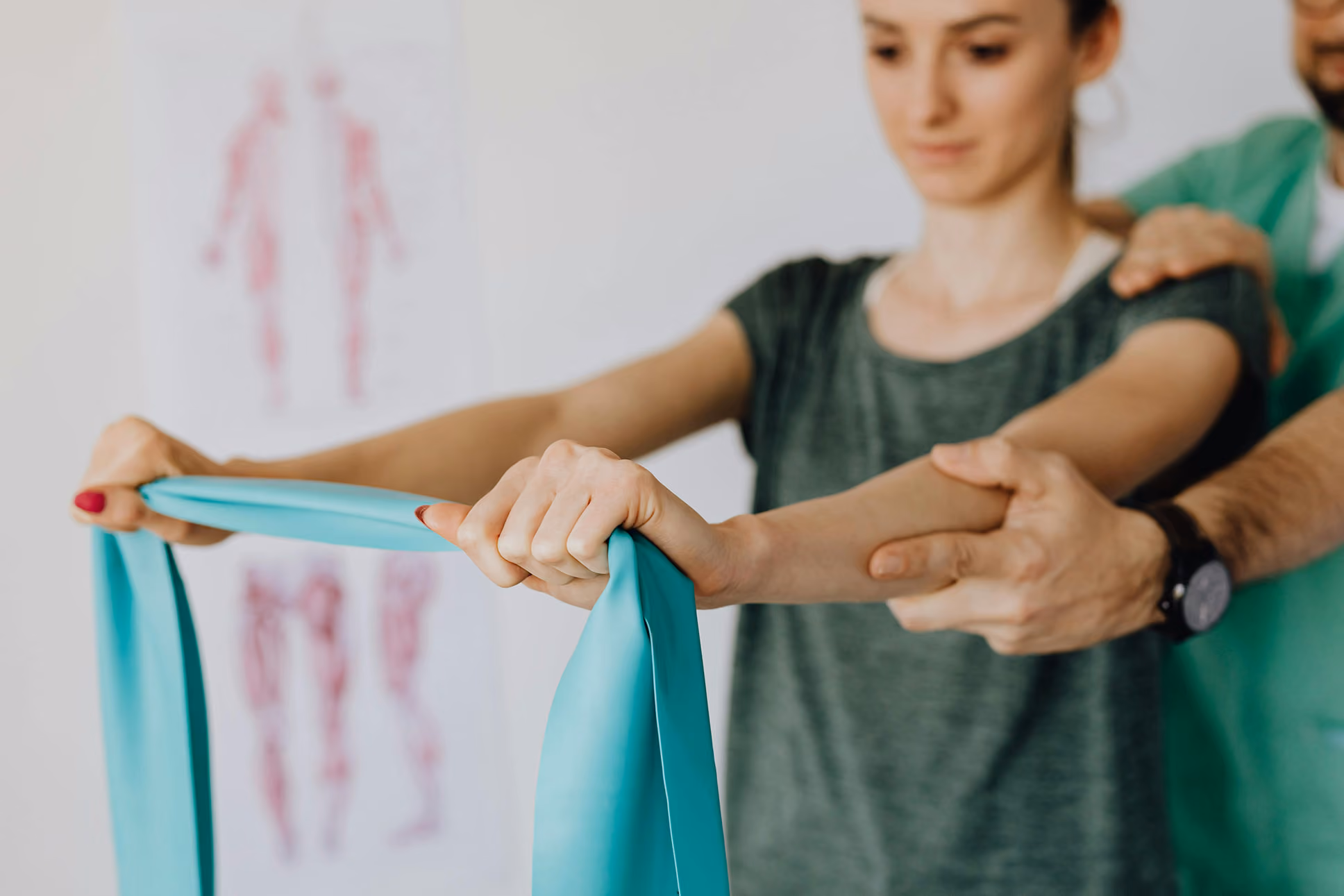 Female patient stretching a resistance band with guidance from a male physical therapist.
