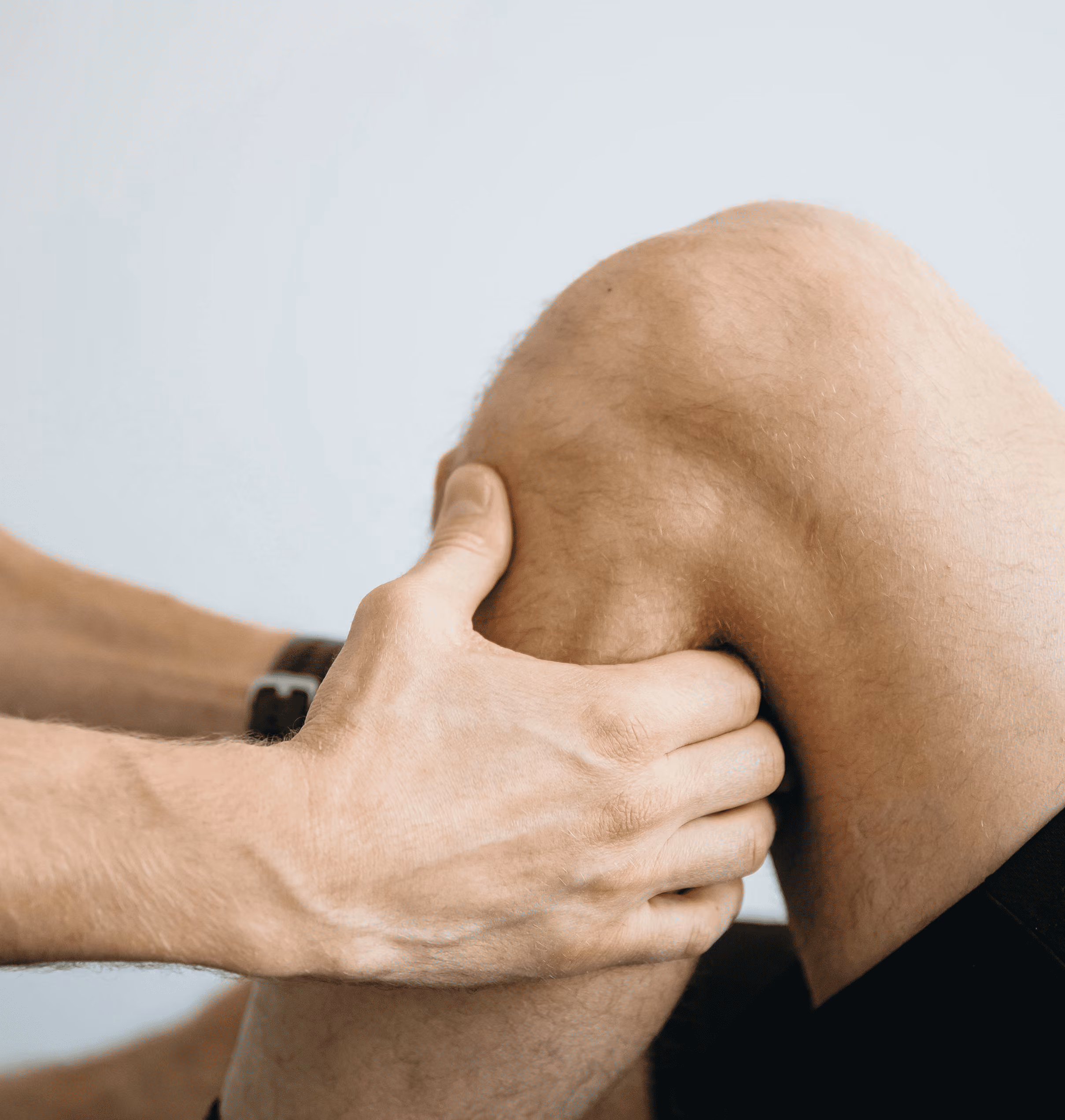 Close-up of a person massaging their bent knee with both hands.
