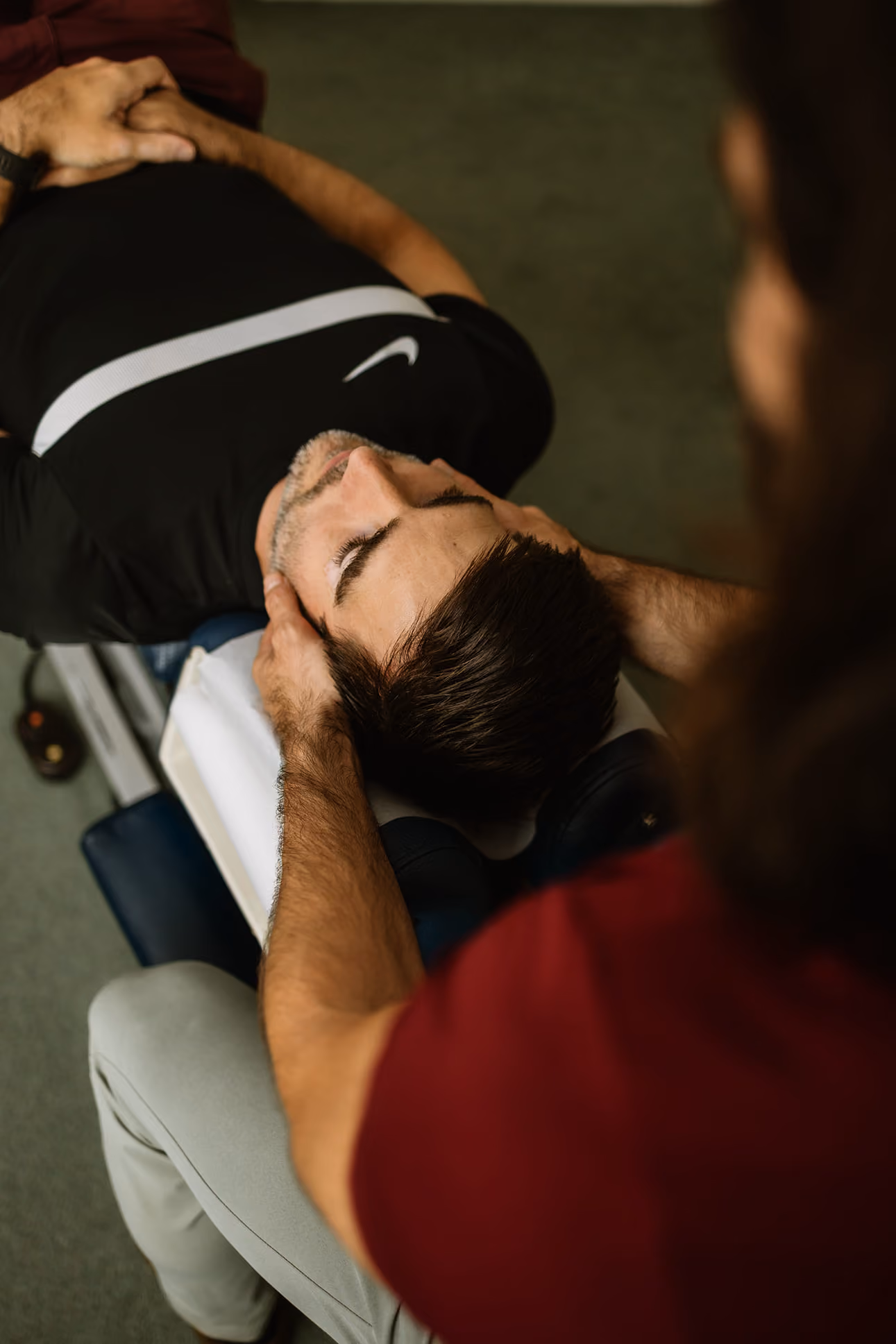 Man lying on a treatment table receiving a neck chiropractic adjustment from a therapist.