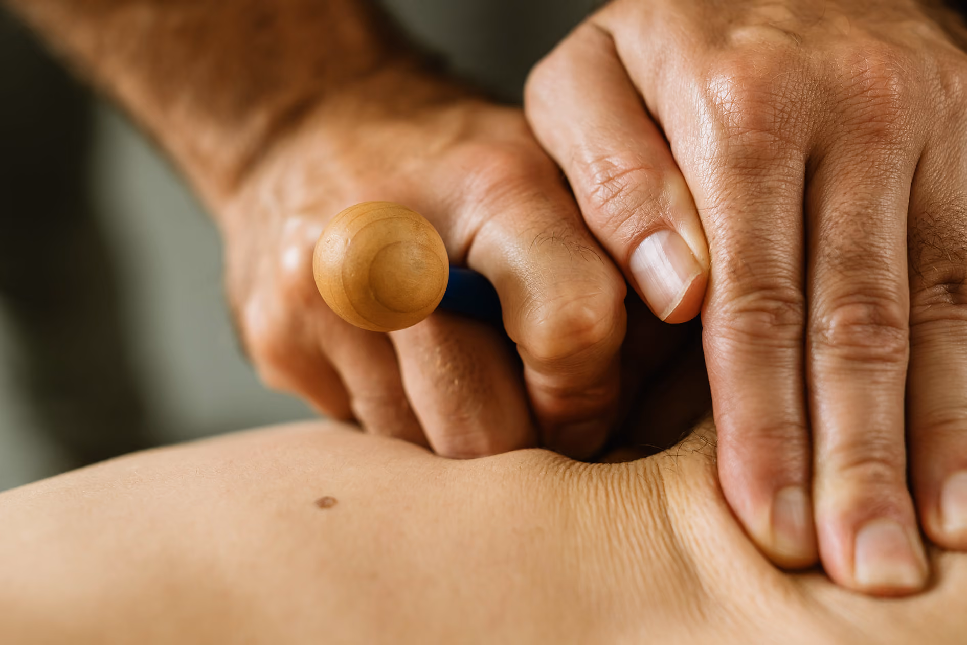 Close-up of hands performing sport massage with wooden tool on bare back skin.