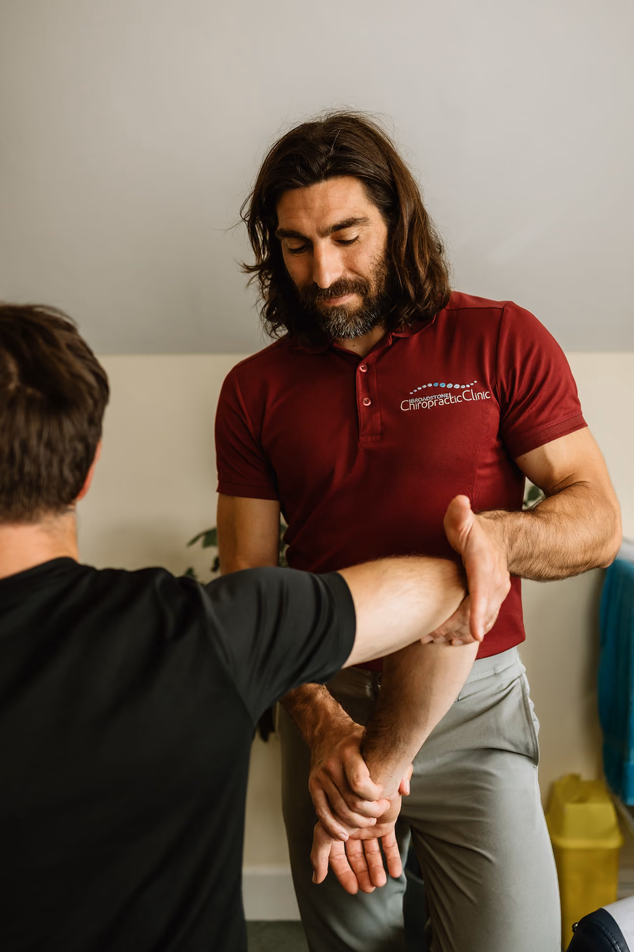 Chiropractor in maroon shirt stretching a patient's arm inside a clinic.