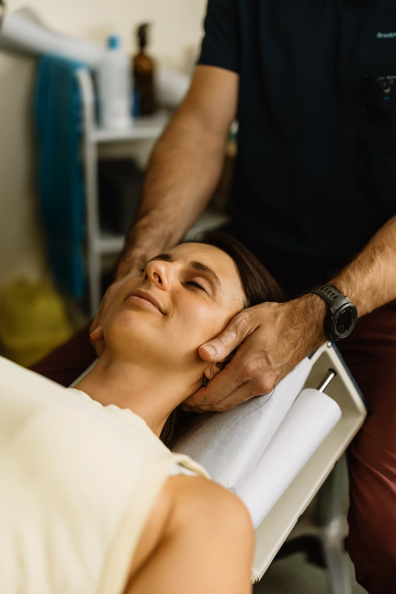 Woman with eyes closed receiving chiropractic neck treatment from a person wearing a black shirt and watch.