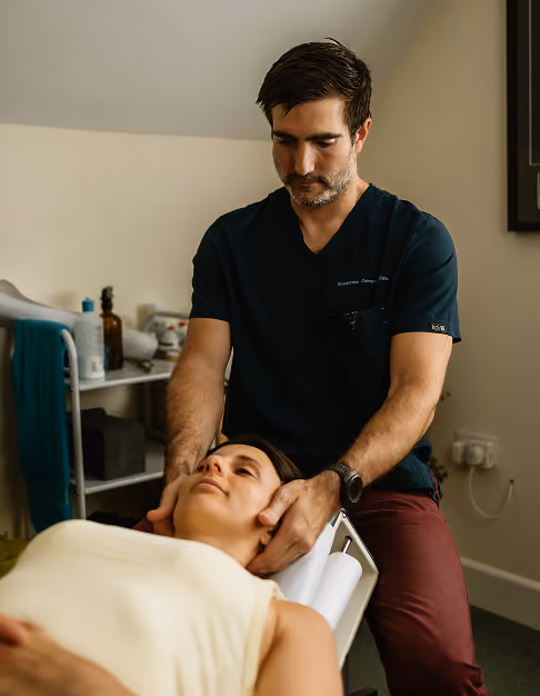 Chiropractor gently holding a woman's neck while she lies on a treatment table in a clinical room.