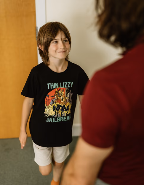 Smiling boy wearing a Thin Lizzy Jailbreak band t-shirt completing a balancing exercise with chiroporactor