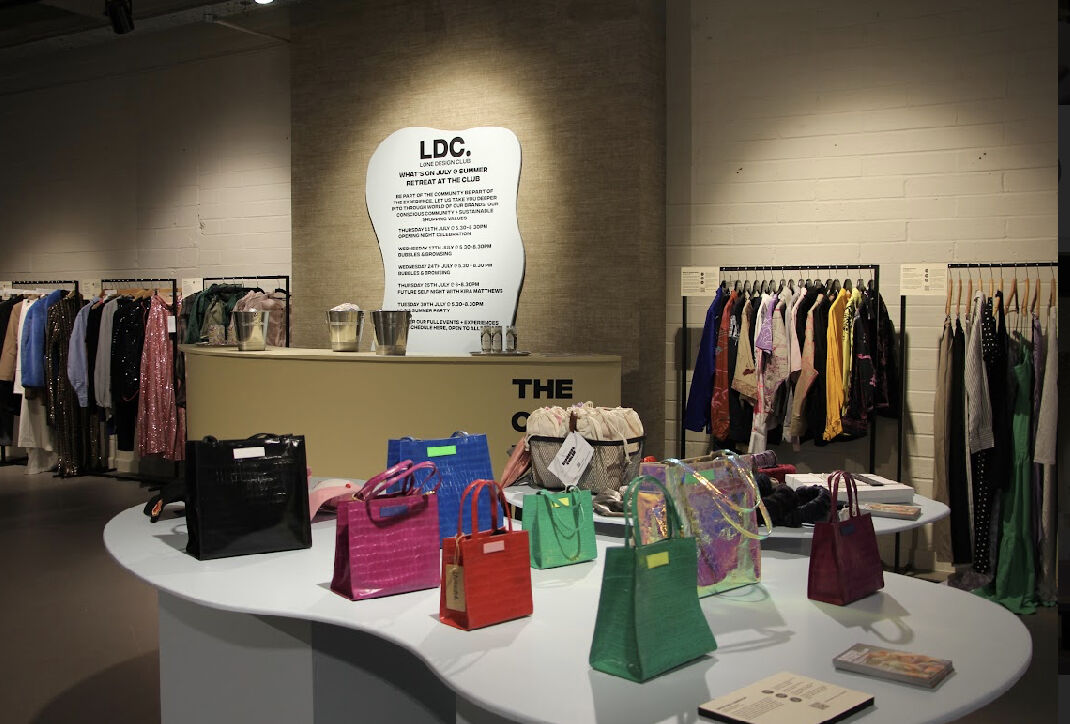 Lone Design Club retail space showcasing designer handbags and clothing, with a softly lit backdrop featuring LDC's mission statement.