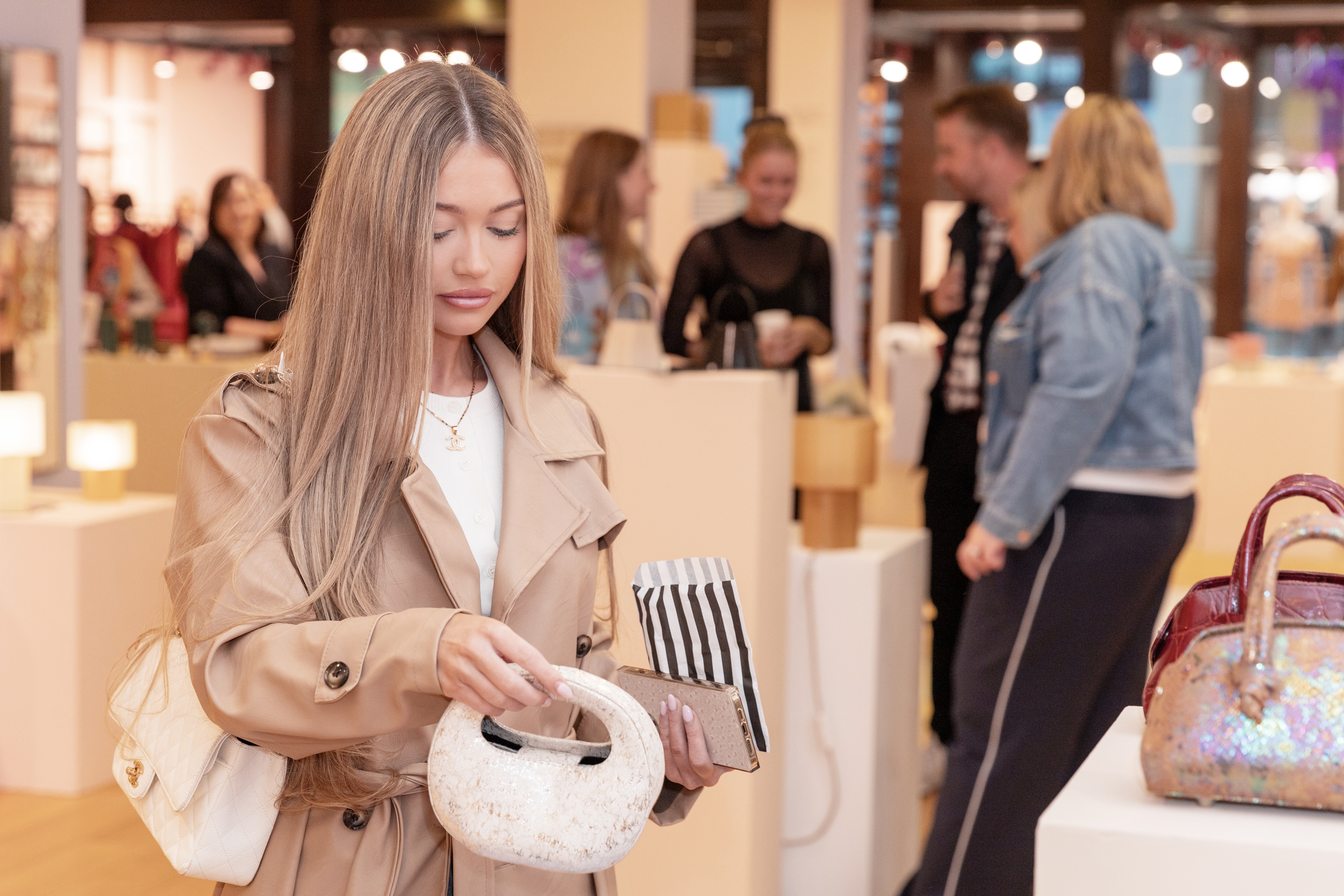 A shopper explores an independent brand’s handcrafted handbag while speaking with a designer at a CO.LAB retail event by Lone Design Club. In the background, emerging brands and designers engage with visitors.