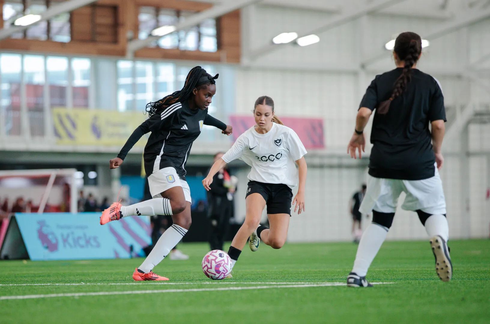 Women soccer players competing for the ball on an indoor field during a match.