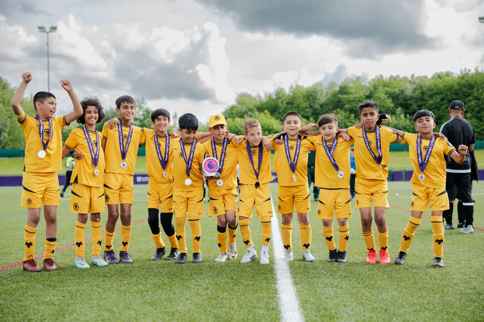 Youth soccer team in yellow uniforms posing with medals and a trophy on a green field.