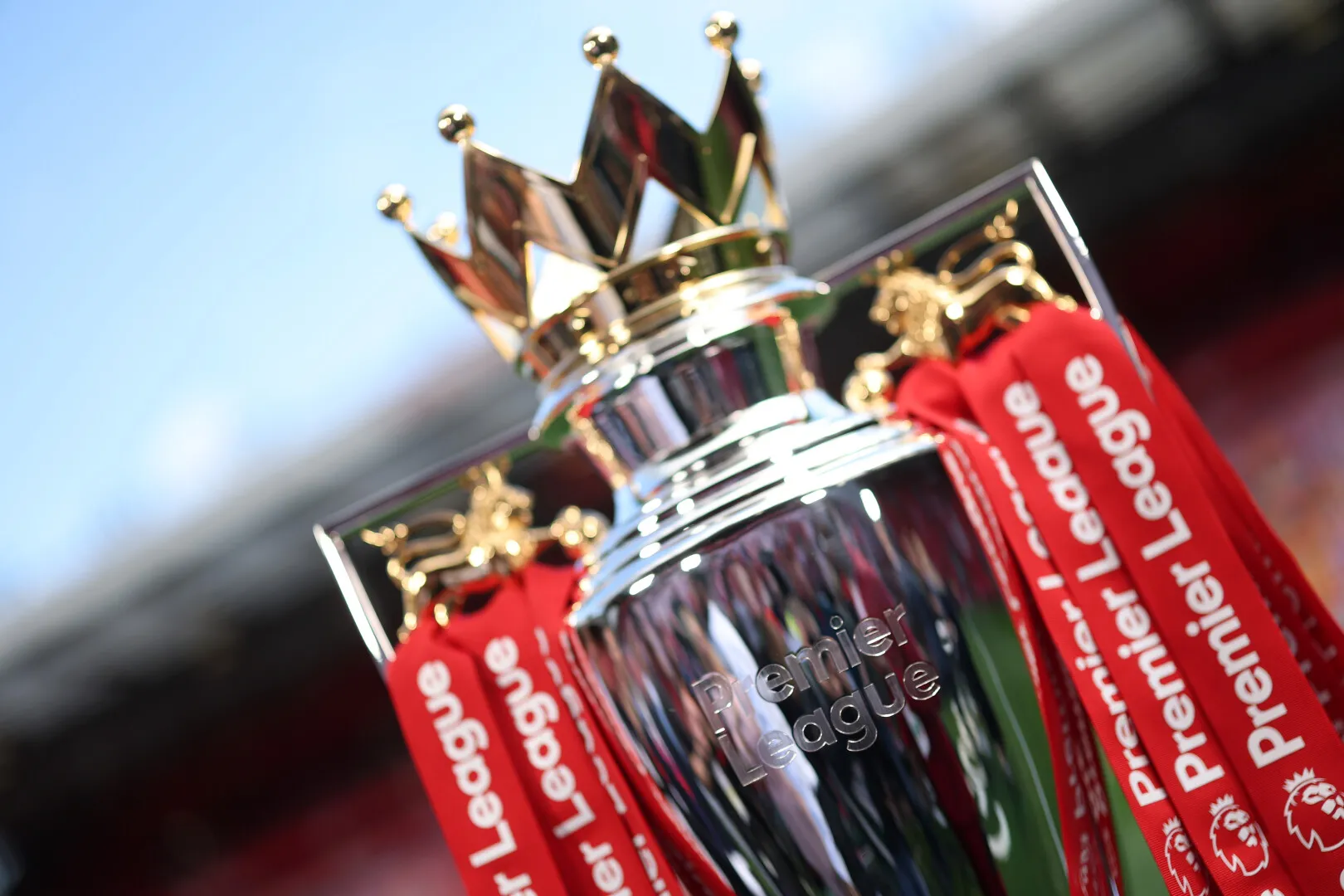 Close-up of the Premier League trophy with red ribbons displaying the league's name.