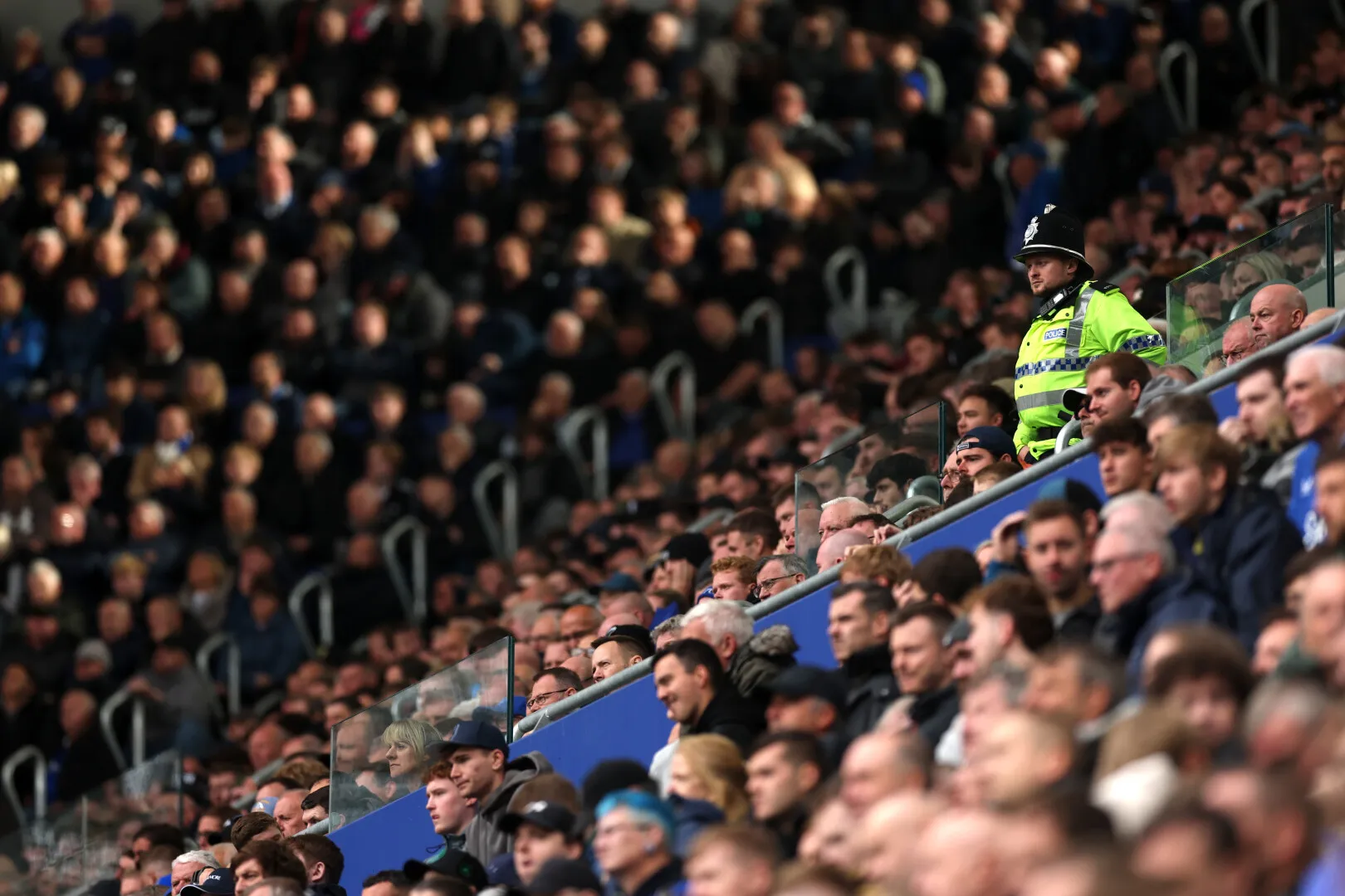 Crowded stadium seating with a police officer in a high-visibility jacket standing among spectators.