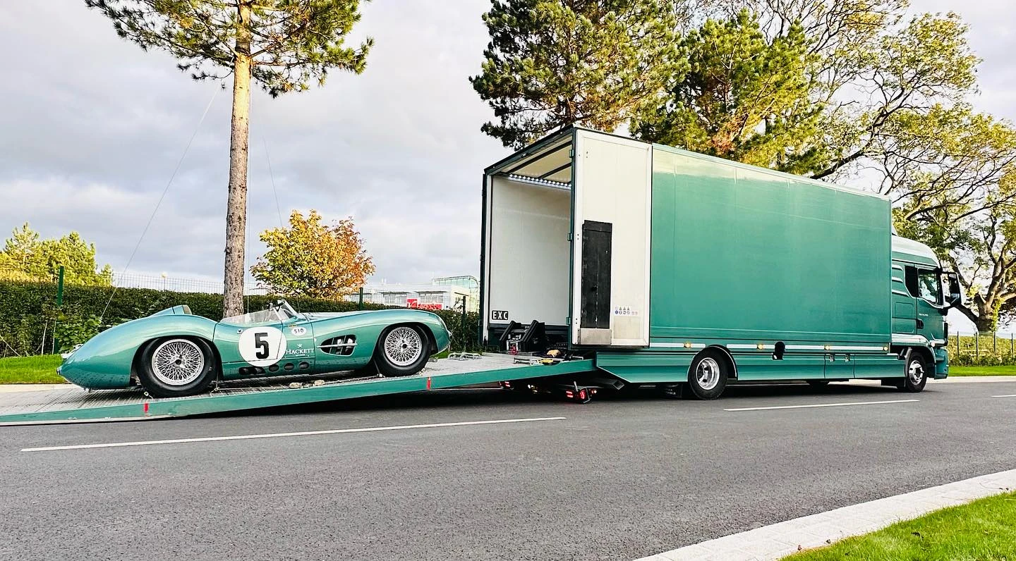 Vintage green race car with number 5 being loaded onto a green transport truck on a road.