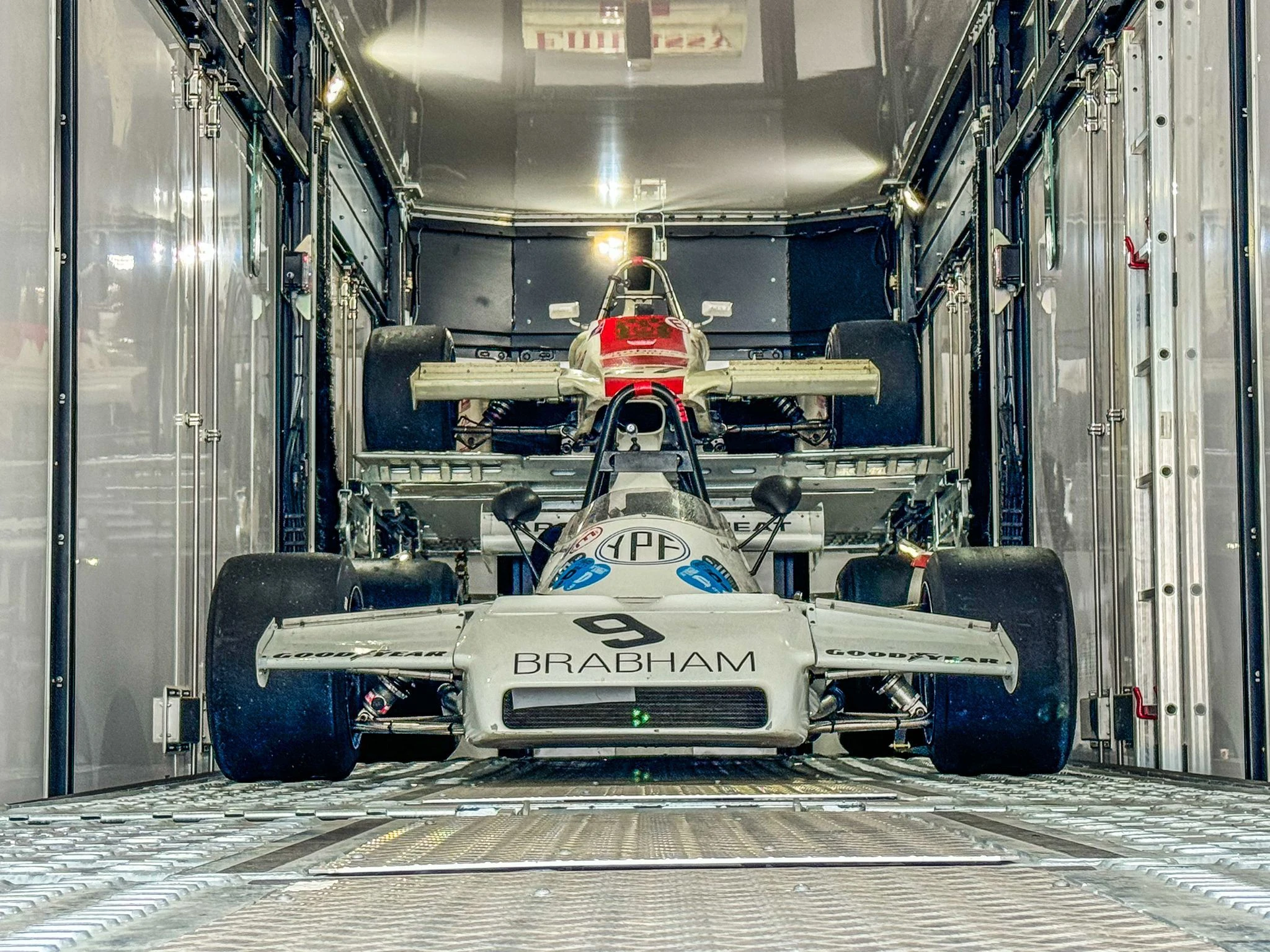 Man polishing a silver classic Aston Martin car with license plate BMT 216A displayed on a raised platform with Bollinger 007 branding.