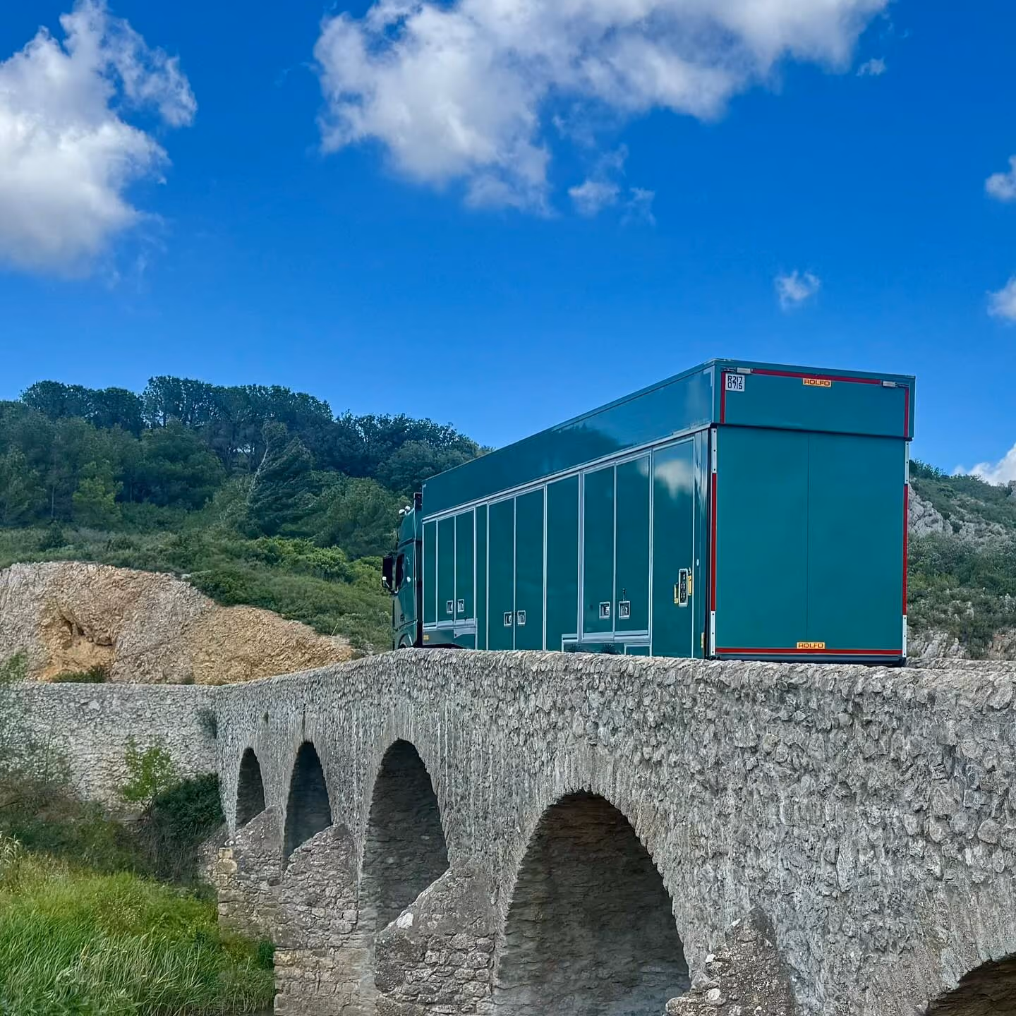 Green DAF semi-truck parked on a snowy mountain road under a clear blue sky.