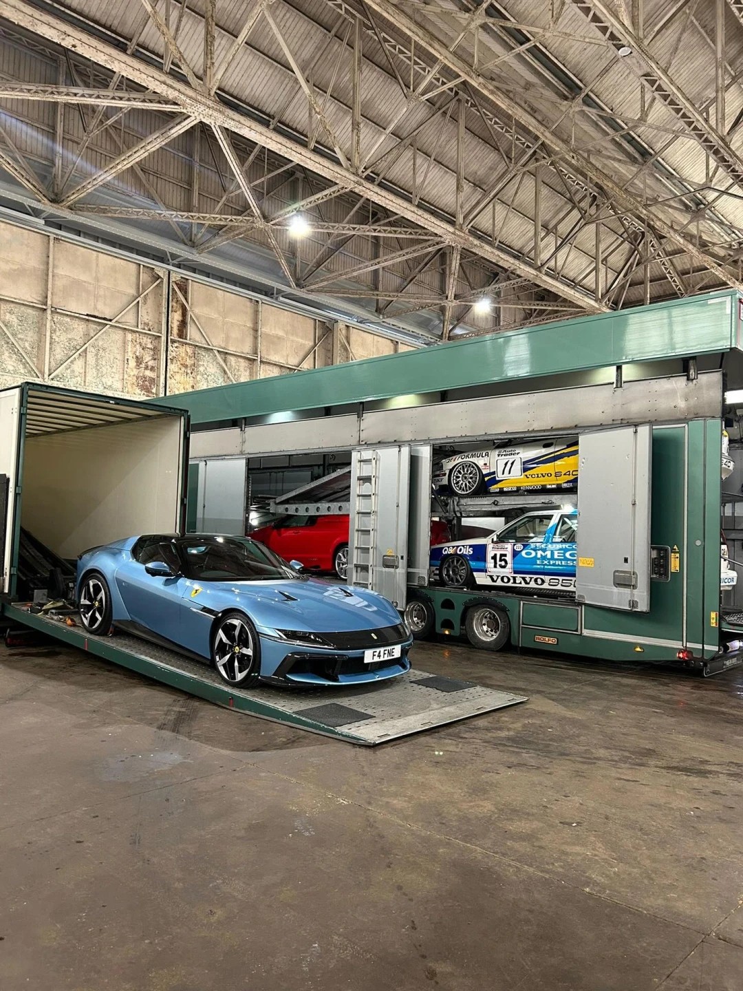 Old moss-covered car with flat tires loaded on a flatbed truck inside a large warehouse.