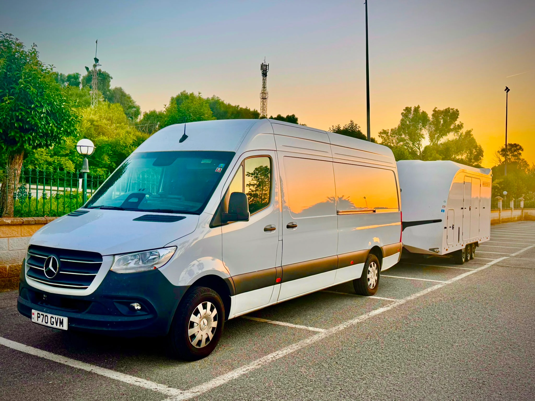 Red sports car with black stripes loaded inside a white enclosed car transporter trailer hitched to a white van.