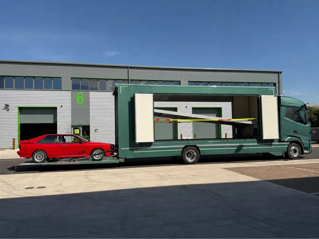 Red sports car with black stripes loaded inside a white enclosed car transporter trailer hitched to a white van.