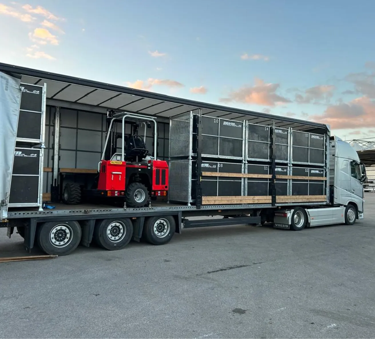 Vintage silver race car loaded on a green enclosed transport truck ramp in front of a building.