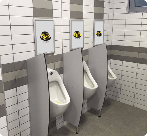 Man in a suit standing in front of a row of modern bronze urinals with screens above displaying a logo and the word 'MEDIA'.
