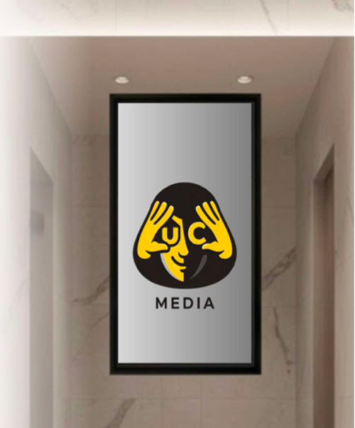 Framed digital screen in a hallway displaying a stylized logo of a face made from two yellow hands forming glasses around the eyes, with the word 'MEDIA' below.