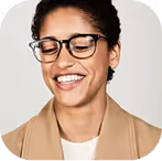 Smiling woman with glasses and short curly hair wearing a beige blazer and white shirt.