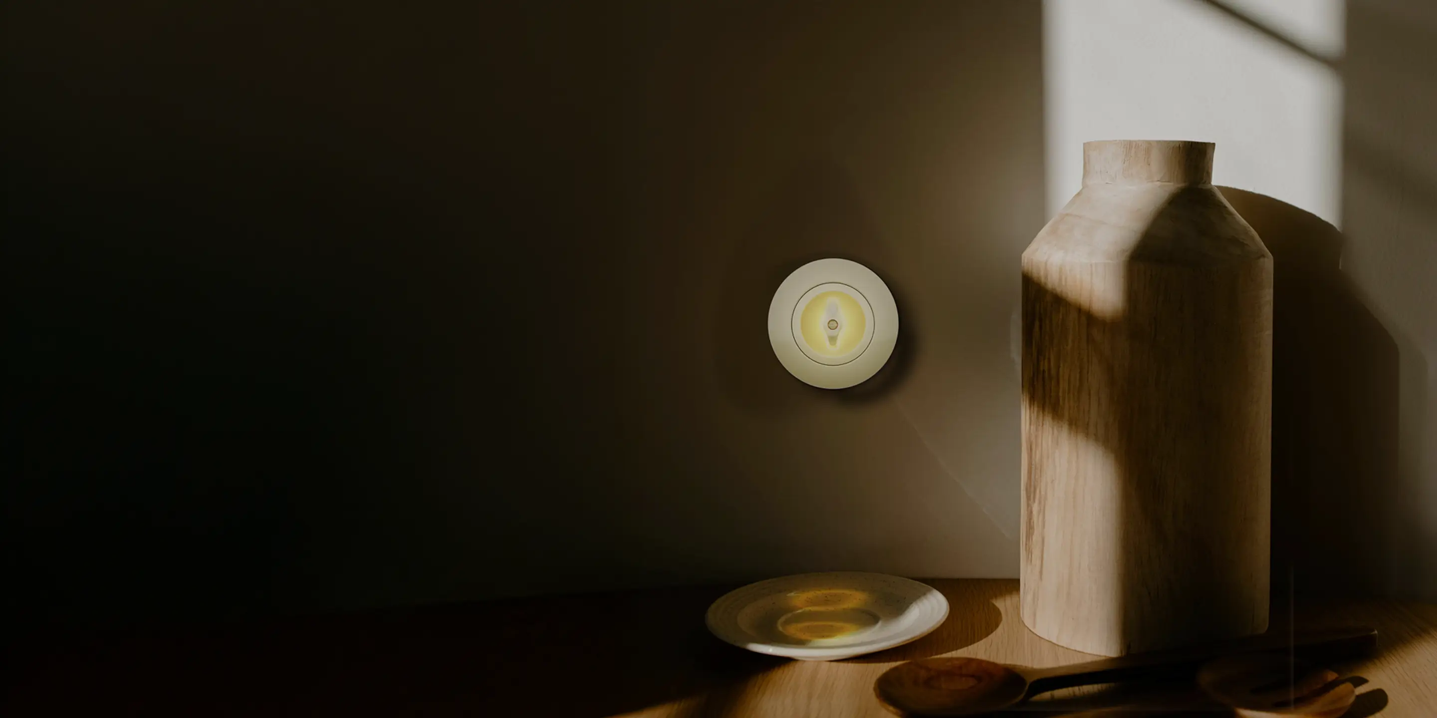 Houten vaas en houten lepels op een tafel met warme zonnestralen en een wandlamp aan de muur.