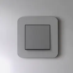 Houten vaas met takken naast twee witte kommen en een lichtschakelaar op een grijze muur.