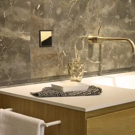 Moderne badkamerkast met houten afwerking, witte blad, gouden kraan en glazen beker op een handdoek.