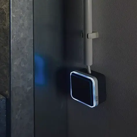 Elektrische schakelaar met een lichtindicator gemonteerd op een donkergrijze muur naast een metalen deurpost.