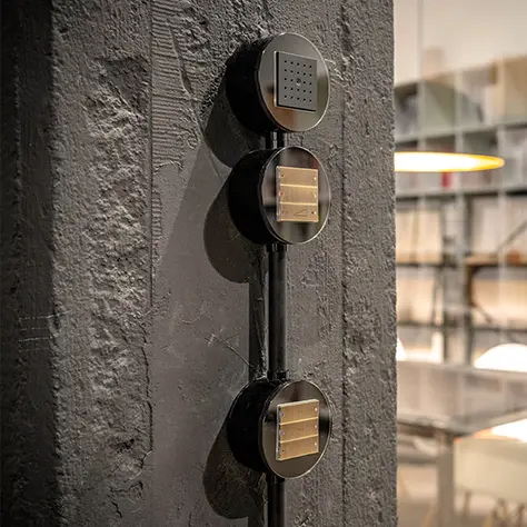 Drie ronde, zwarte schakelaars met enkele schakelaars gemonteerd op een ruwe, donkere muur in een industriële ruimte.