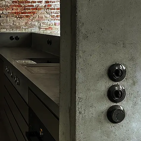 Moderne keukenhoek met zwarte kasten, donker aanrechtblad en ruwe bakstenen achterwand.