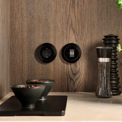 Twee zwarte stopcontacten ingebouwd in houten keukenwand met peper- en zoutmolens en zwarte kommen op witte keukenplaat.