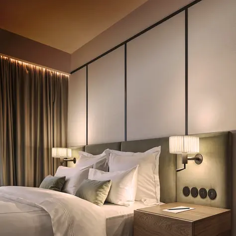 Sfeervolle slaapkamer met een groot bed, meerdere kussens, een nachtkastje met boek en wandlampen aan een beklede hoofdeind.