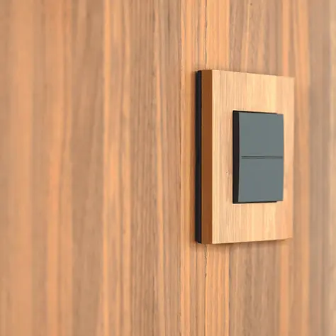 Zwarte lichtschakelaar gemonteerd op een houten wandpaneel met een lichte houtafwerking.