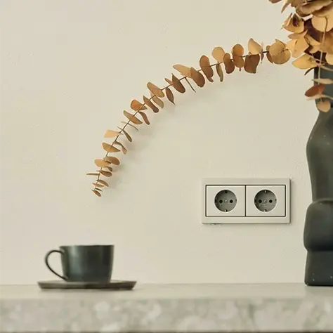 Zwarte kopje en schotel op een marmeren oppervlak met een tak van gedroogde eucalyptus en een dubbele witte stopcontact op een lichte muur.