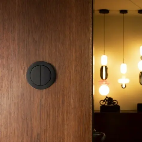Ronde zwarte schakelaar op een houten deur met warme hanglampen en zachte verlichting op de achtergrond.