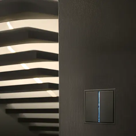 Moderne zwarte lichtschakelaar op een donkere muur met zicht op zwevende traptreden in de achtergrond.