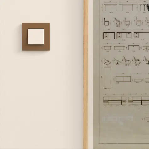 Een vierkante lichtschakelaar met een bruine omlijsting aan een witte muur naast een houten lijst en een raam met bouwtekeningen.
