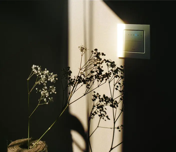 Een zonnige scene met invallend licht op een aluiminium touch dimmer en een bloemtak op de voorgrond