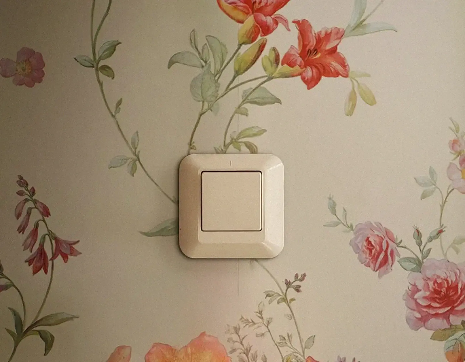 Een gelige ouderwetse lichtschakelaar op een bloemetjesbehang met het licht van rechts