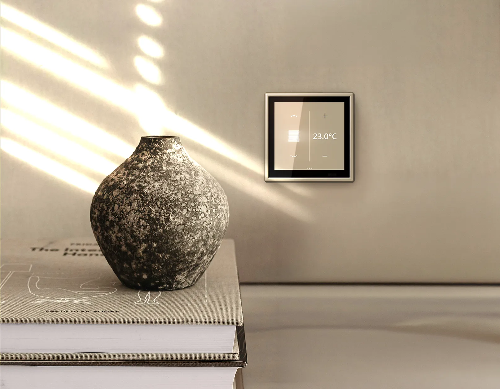 Een zonnige scene in beige met zonlicht van links door de luxaflex, een stapel boeken waarop een aardewerk potje staat en een JUNG LS-Touch paneel op de wand