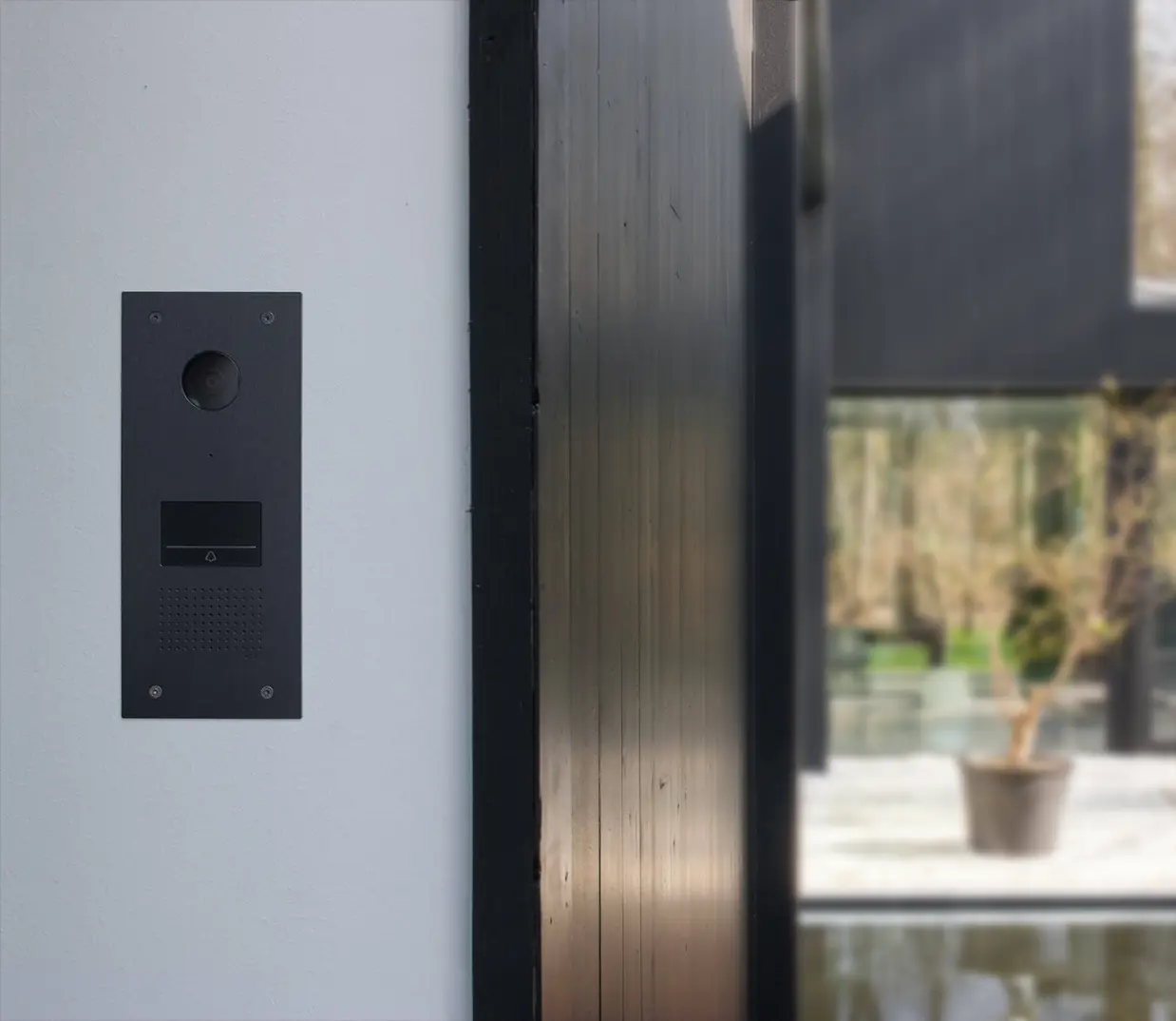 Een deurbel-buitenpost voor Niko Home Control, uitgevoerd in zwart staal en gemonteerd op de buitenmuur van een moderne woning