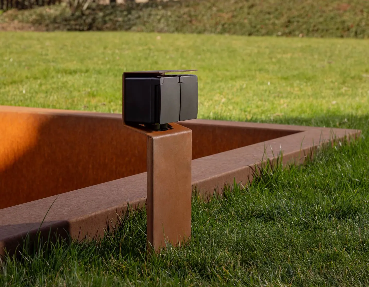 Niko tuinpaal Essential uitgevoerd in Cortenstaal, geplaatst in een groene tuin