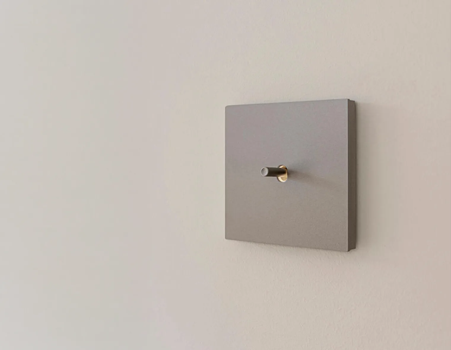 NIko Toggle® in de kleur alu blue grey brushed met navigatie lichtje bij de schakelknop, op een licht grijze muur