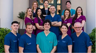 Group portrait of medical professionals in scrubs standing outside a building.