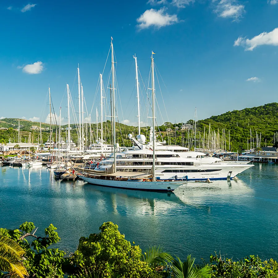 Yachts and sailboats docked in a marina with green hills and blue sky in the background.