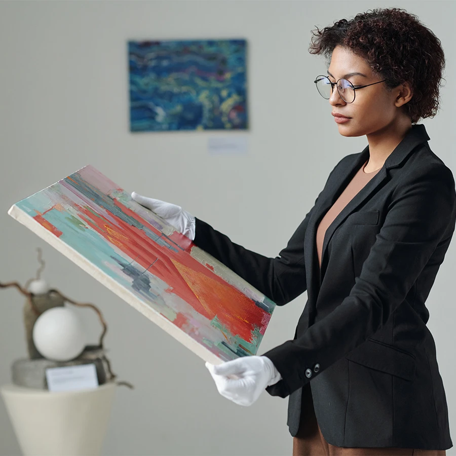 Woman wearing white gloves and glasses examining an abstract red and teal painting in an art gallery.