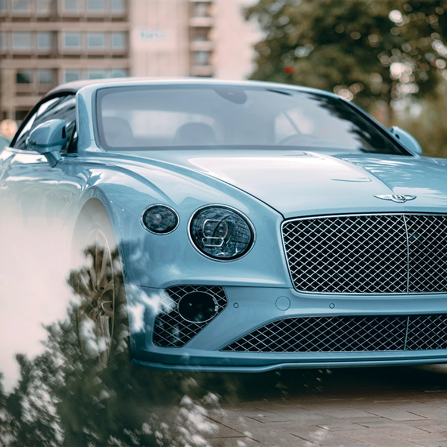 Front view of a light blue Bentley luxury car with a chrome grille and round headlights parked outdoors.