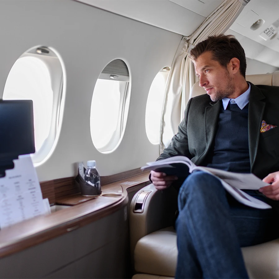 Man in business attire sitting in a private jet cabin reading documents and looking out the window.