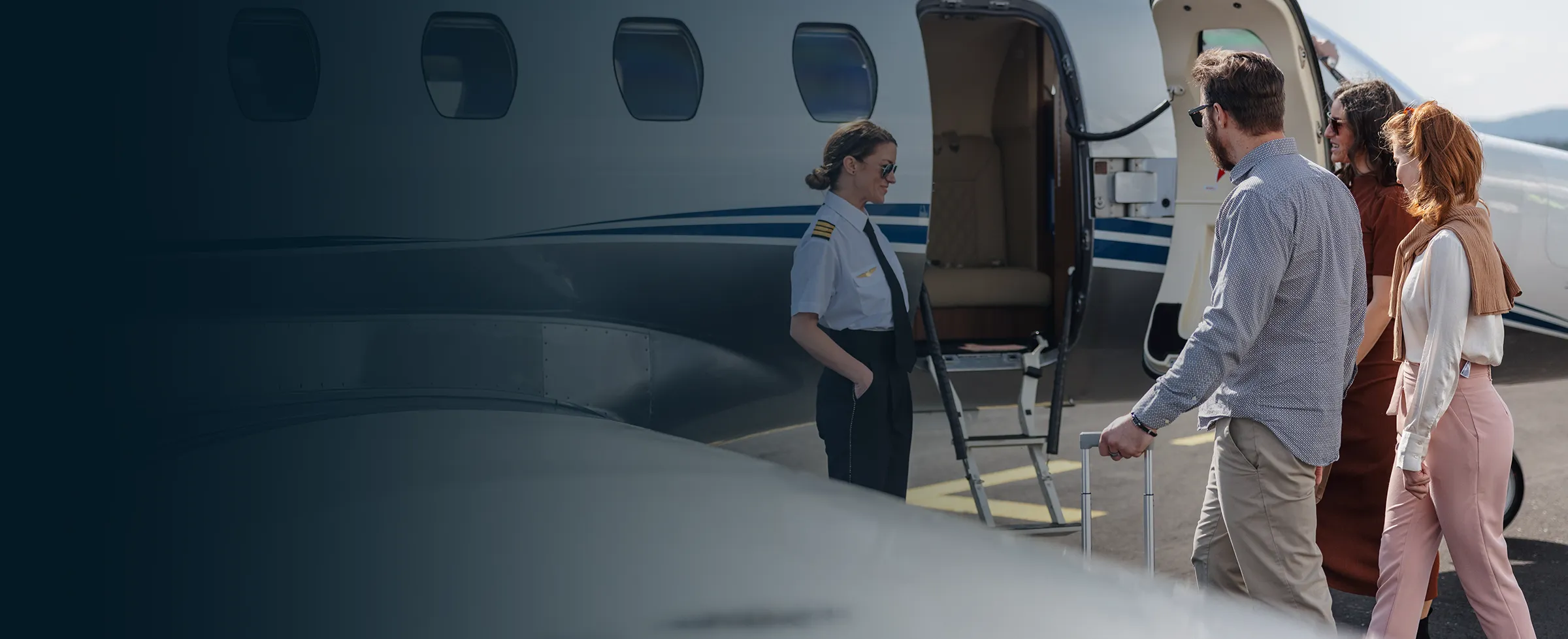Three passengers walking towards a private plane greeted by a female pilot standing at the open door.