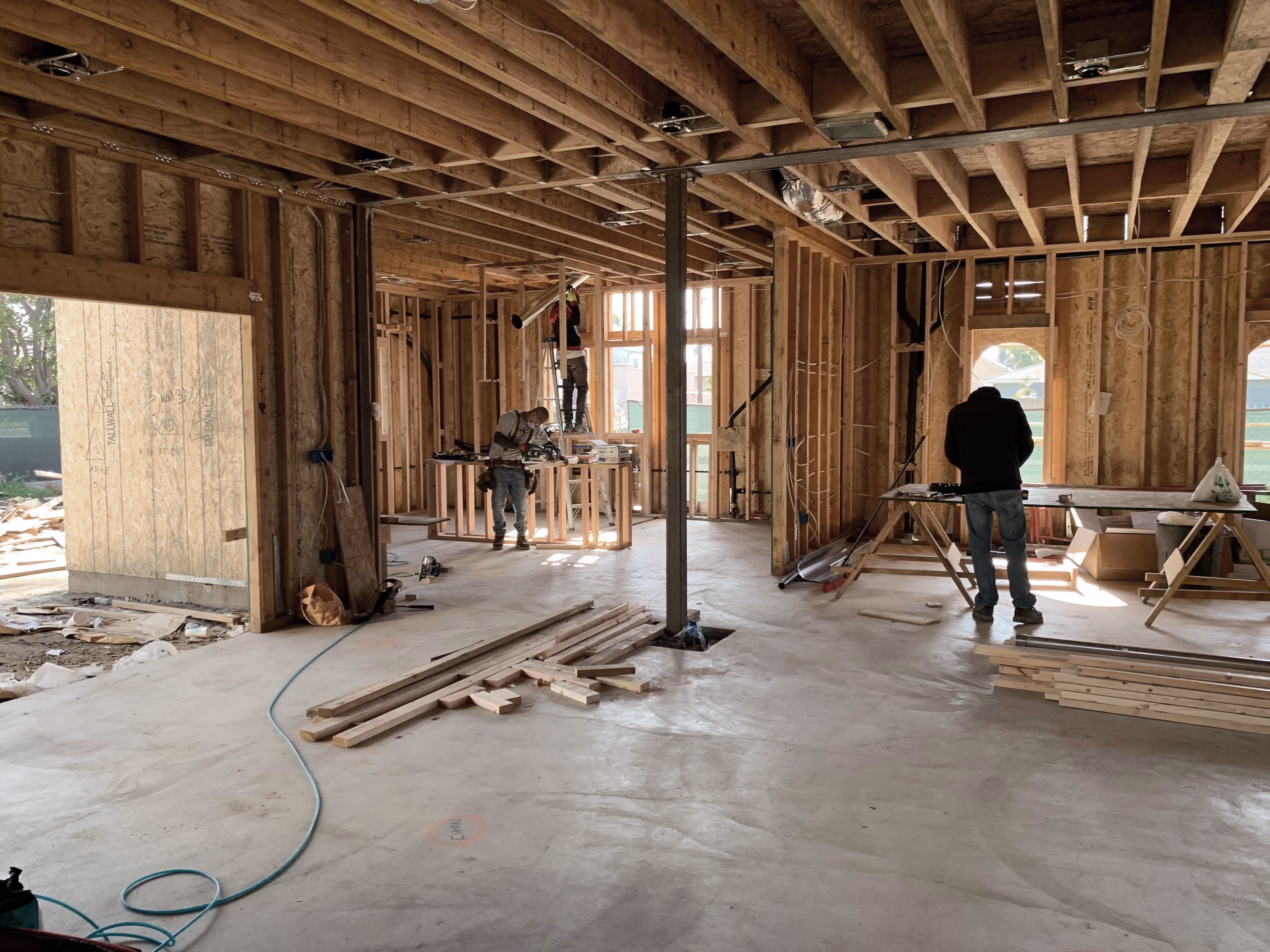 Three workers inside a wooden framed house under construction with tools and lumber scattered on the floor.